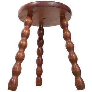 May include: A wooden stool with three legs. The legs are round and have a series of bumps along their length. The stool is made of dark brown wood.