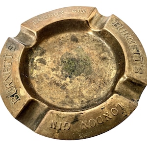 May include: A brass ashtray with the text "BURNETT'S LONDON GIN" embossed around the rim.