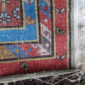 May include: Close-up of the edge of a red, blue, and yellow patterned rug with white fringe.