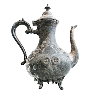 Puede incluir: Una tetera de plata antigua con intrincados diseños florales y un acabado desgastado. La tetera tiene un cuerpo redondeado, un pico curvo y una tapa con un pomo.