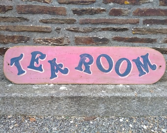 May include: A vintage wooden sign painted pink with the words "Tea Room" in blue lettering.