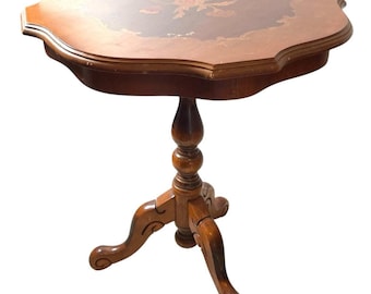 Op de afbeelding: Een vintage houten bijzettafel met een geschulpte rand en een bloemeninleg op het tafelblad. De tafel heeft een donkerbruine afwerking en een driepotige basis. De tafel is ongeveer 71 cm hoog.
