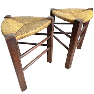 Può includere: Due sgabelli triangolari in legno con sedute in paglia intrecciata. Gli sgabelli hanno una finitura marrone scuro e sono realizzati in legno robusto.