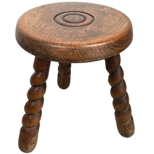 May include: A wooden stool with a round top and three twisted legs. The top has a carved circle design.