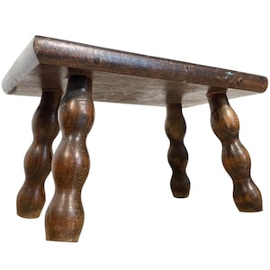 May include: A dark brown wooden stool with four turned legs. The legs are shaped like a series of rounded bumps.