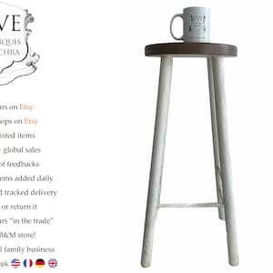 Peut inclure: Tabouret en bois blanc avec un dessus rond. Le tabouret a quatre pieds et une finition peinte en blanc. Une tasse blanche avec le texte "EVE ANTIQUIS PULCHRA" est posée sur le dessus du tabouret.