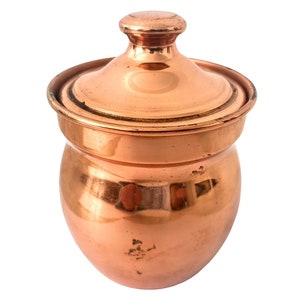 May include: A copper jar with a lid. The jar is round and has a slightly flared top. The lid is domed and has a knob on top.