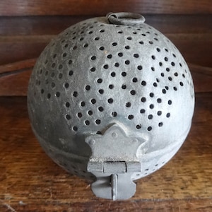 May include: A vintage, silver-colored, round, metal strainer with a hinged lid and a handle. The strainer has a pattern of small holes throughout the surface.