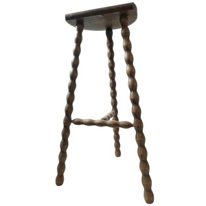 Pode incluir: Banqueta de bar de madeira marrom escuro. Possui assento curvo e quatro pernas torneadas com design espiral. Uma barra horizontal conecta as pernas para maior estabilidade. Estilo vintage.