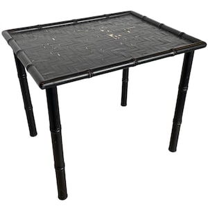 Puede incluir: Mesa auxiliar de bambú negro con tapa tejida. La mesa tiene cuatro patas y está hecha de bambú natural.