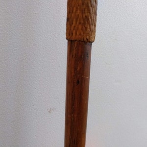 May include: A close-up of the top of a wooden walking stick with a woven brown top.