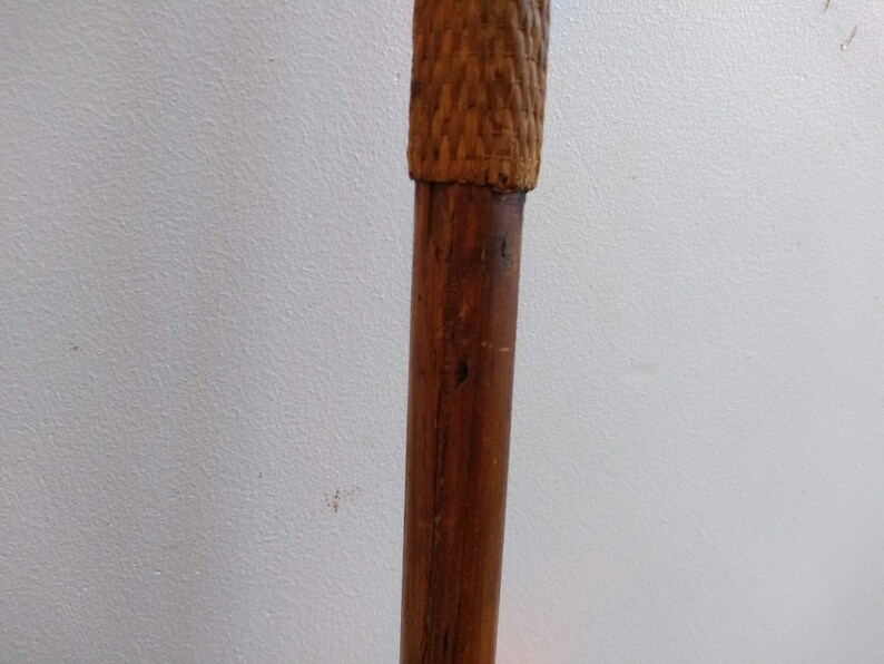 May include: A close-up of the top of a wooden walking stick with a woven brown top.