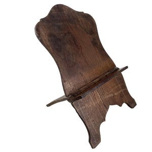May include: A dark brown wooden book stand with a decorative top and a shelf for holding a book. The stand is made of solid wood and has a rustic look.