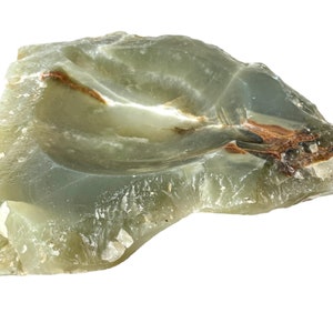 Peut inclure: Un bol en pierre naturelle vert et brun avec une surface rugueuse et irrégulière. Le bol est sculpté dans une seule pièce de pierre et a une forme naturelle et organique.