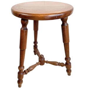 Op de afbeelding: Een ronde houten kruk met drie gedraaide poten en een eenvoudig ontwerp. De kruk is gemaakt van donkerbruin hout en heeft een gladde, gepolijste afwerking.