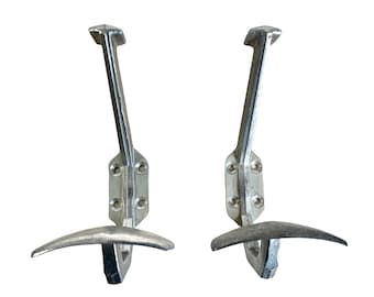 May include: Two silver metal coat hooks with a curved design. The hooks are mounted on a wall.