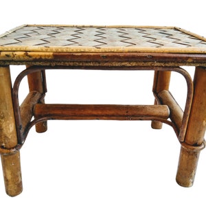 May include: A small, brown, woven bamboo stool with a rectangular top. The top is made of woven bamboo strips and has a chevron pattern.