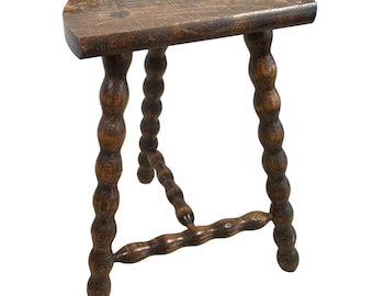 May include: A dark brown wooden stool with a half-round seat and turned legs. The legs are made of a series of small, rounded knobs.