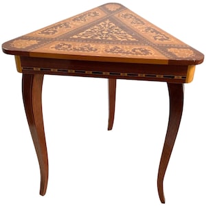 Puede incluir: Una mesa de madera triangular con intrincada incrustación de marquetería en un patrón floral. La mesa tiene tres patas con un diseño curvo.