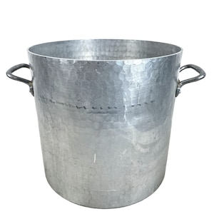 May include: A large, silver, hammered aluminum stock pot with two handles. The pot is empty and has a slightly textured surface.