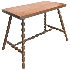 May include: A wooden table with a rectangular top and turned legs. The table has a warm brown color and a rustic design. The legs are connected by a horizontal stretcher. The table is suitable for various uses.