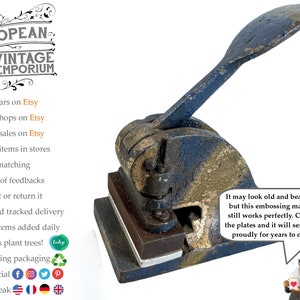 May include: Vintage metal embossing machine with a black handle and a worn, aged surface. The machine has a rectangular base and a lever that is used to operate the embossing plates. The machine is in good condition and appears to be functional.