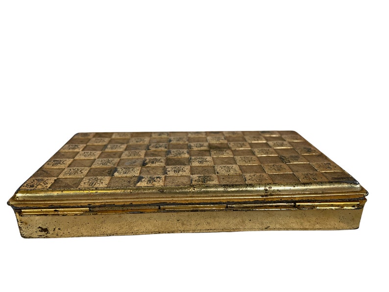 May include: A gold metal box with a checkered pattern on the lid. The box has a hinged lid and is closed.