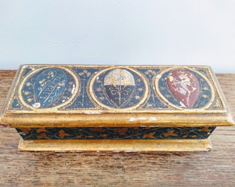 May include: A rectangular wooden box with a gold-painted finish. The top of the box is decorated with three oval-shaped panels, each featuring a different design. The panels are painted in shades of blue, gold, and red. The box is approximately 10 inches long.