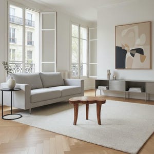 May include: A modern living room with a light gray sofa, a small wooden coffee table, and a large abstract painting. The room has large windows and a neutral color palette, with a white rug and a black side table.