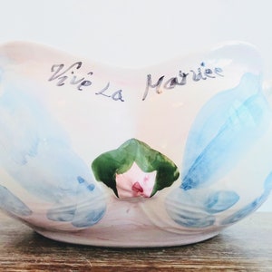 Può includere: Una ciotola in ceramica bianca con due manici, dipinta con fiori blu e rosa e le parole "Vive La Mariée".