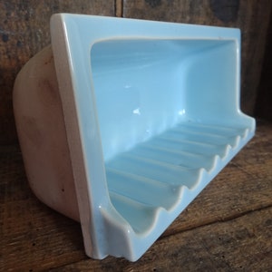 May include: A light blue ceramic soap dish with a wavy edge and six ridges on the bottom. The dish is designed to hold a bar of soap.