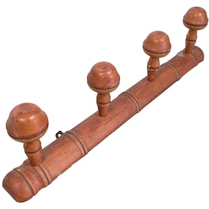 Może przedstawiać: Drewniany wieszak na ubrania z czterema haczykami. Wieszak wykonany jest z jasnobrązowego drewna i ma naturalne wykończenie. Haczyki mają kształt małych grzybów i są wykonane z tego samego drewna co wieszak.