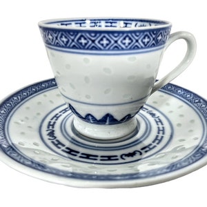 Può includere: Un set da tè in porcellana bianca con un motivo floreale blu e bianco. La tazza ha un manico e il piattino ha un bordo ondulato.