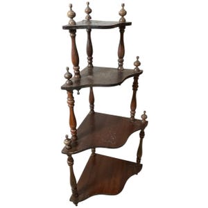 May include: A vintage, dark brown corner shelf with four triangular shelves. The shelves are supported by turned wooden posts with decorative finials. The wood has a rich, aged appearance, suggesting it is antique.
