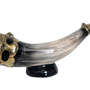 Könnte beinhalten: Ein Trinkhorn aus Keramik mit einem schwarz-weißen Bemalung. Das Horn hat einen goldenen Rand und einen schwarzen Sockel.