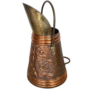 May include: A copper and brass coal scuttle with a hammered finish and an embossed design. The scuttle has a handle and a hinged lid.