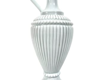 May include: A white ceramic pitcher with a fluted design and a rounded base. The pitcher has a handle and a spout.