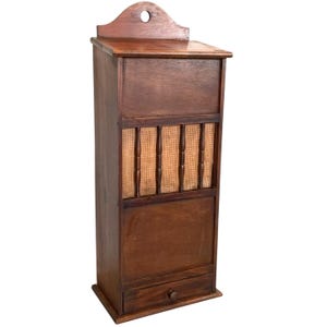 Op de afbeelding: Een vintage houten wandkast met een kleine lade, een geweven draadgaasgedeelte en een scharnierende deur. De kast is donkerbruin en heeft een verweerde afwerking.