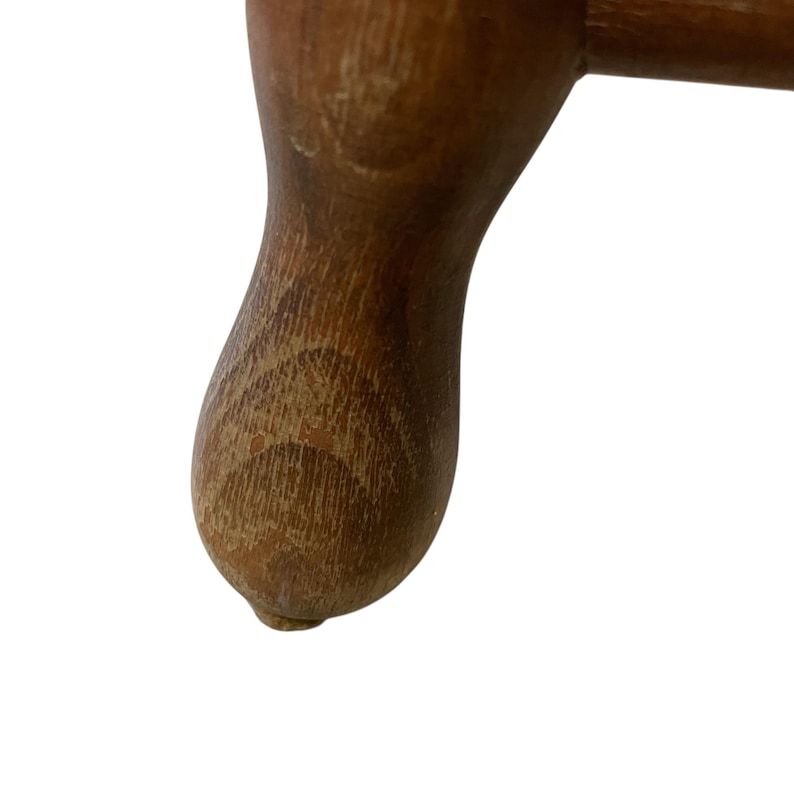 K&ouml;nnte beinhalten: Nahaufnahme eines Holzm&ouml;belfu&szlig;es. Das Bein ist dunkelbraun mit sichtbarer Holzmaserung und einem abgerundeten, bauchigen Ende. Das Holz weist Gebrauchs- und Altersspuren auf.