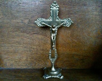 May include: A silver-toned metal crucifix with a figure of Jesus Christ on the cross. The crucifix is on a stand with a decorative base.