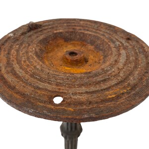 May include: A rusty metal base with a circular top and a central hole. The base has a textured surface and is likely part of a vintage lamp or stand.