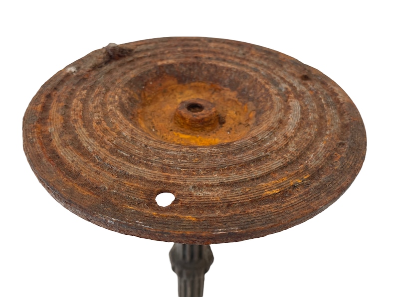 May include: A rusty metal base with a circular top and a central hole. The base has a textured surface and is likely part of a vintage lamp or stand.