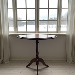 Peut inclure: Une table d'appoint de style ancien, brun foncé, avec un plateau festonné unique. La table a un seul pied central avec trois pieds. La table mesure environ 71 cm de haut.