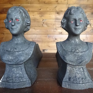 Puede incluir: Un par de soportes de chimenea de hierro fundido negro en forma de busto de mujer. Los soportes tienen un diseño detallado y están en buen estado.