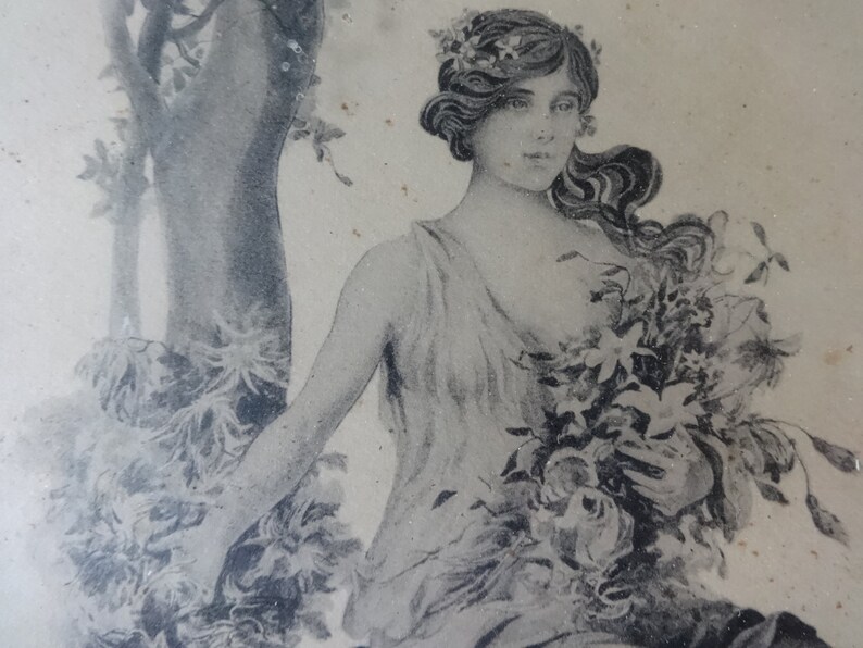 May include: A black and white vintage illustration of a woman with long flowing hair wearing a floral crown and a flowing gown. She is holding a bouquet of flowers in her hands.