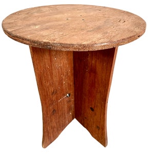 Puede incluir: Un taburete de madera con una parte superior redonda y tres patas. El taburete está hecho de madera natural de color marrón claro.