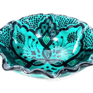 Può includere: Una ciotola in ceramica blu turchese con un bordo ondulato e intricati disegni floreali neri. La ciotola è smaltata e ha una finitura lucida.