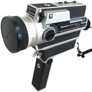 Puede incluir: Cámara de cine vintage Sankyo Super CME 660 Hi-Focus, plateada y negra. Cuenta con un objetivo zoom, una tapa de objetivo negra y el logotipo de Sankyo. El texto indica "Sankyo Super CME 660 Hi-Focus".
