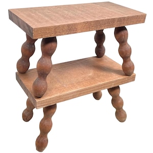 May include: A two-tiered wooden shelf with a natural brown finish. The shelf has four legs with a unique rounded design.