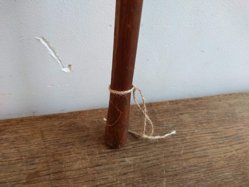 May include: A close-up of a wooden dowel rod with a natural finish. The rod is tied with a piece of twine near the bottom.